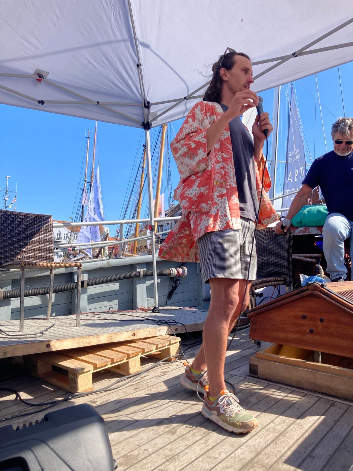 Cole pitching Walt in a kimono on a ship at Folkemødet on Bornholm, with sailboats in the background